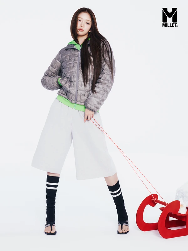 Full-length Millet campaign photograph with a silver-grey quilted jacket, green hoodie, white shorts and red sled.