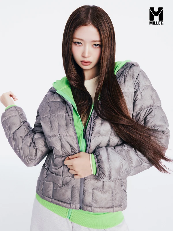 Close-up Millet campaign photograph showing a silver-grey quilted jacket layered over a vivid green hoodie.