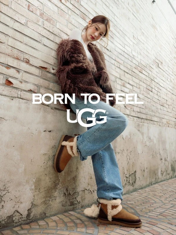 UGG campaign portrait beside a brick wall, with a brown textured jacket, blue jeans and shearling-trimmed boots.