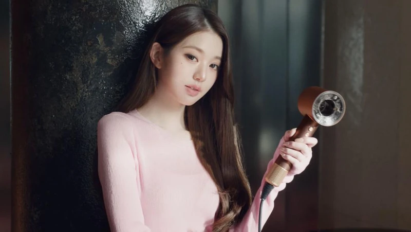 A softly lit portrait in pink knitwear holding a metallic hairdryer