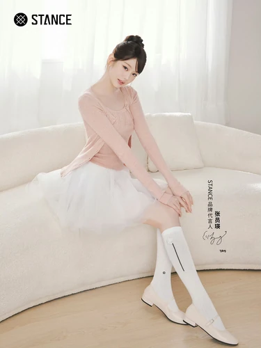 STANCE campaign photograph on a cream sofa, with pink knitwear, a white skirt and knee-high socks