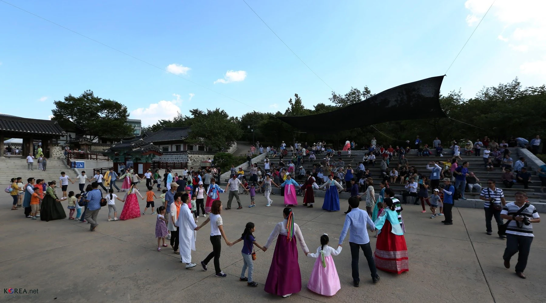 Visitors and performers holding hands in a large circle at Namsangol Hanok Village