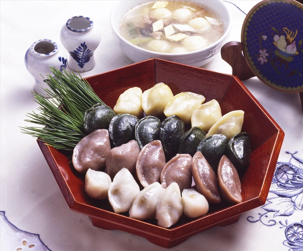 Colourful songpyeon arranged on a tray beside pine needles