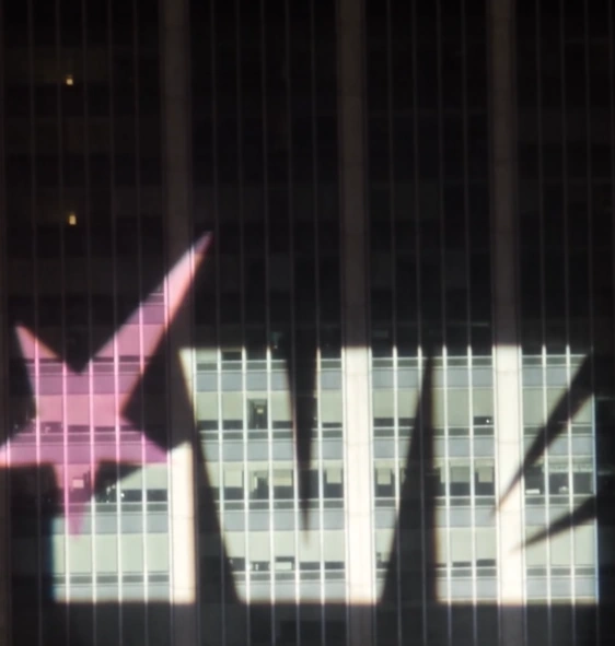 IVE logo and a pink star projected onto a dark building in the Looks Can Kill teaser