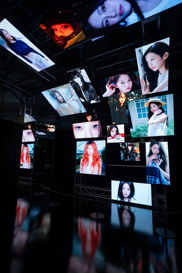 A dark mirrored exhibition space filled with illuminated photographs and suspended screens