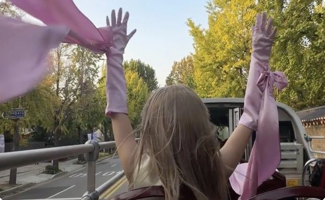 A caped figure with raised arms on an open-top bus