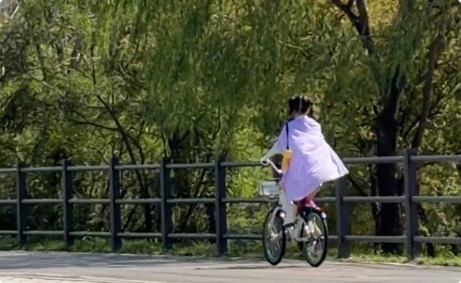 A caped cyclist on a tree-lined riverside path